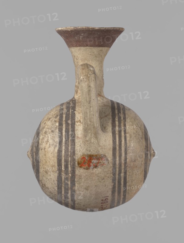 Cypriot gourd jug, A small vessel with a barrel-shaped gourd-shaped body, without a foot, with a spherical bottom. The center is marked with a small protruding point on both short sides. A single handle on the long side, mounted at the greatest bulge of the body and at the base of the neck, bent at a right angle. Quite long neck, strongly flaring, conical spout. Neck and handle slightly offset from the vessel axis; the handle is mounted at a slight angle, with a very clear trace of finger pressure on the right side where it is attached to the neck. Reddish-brown clay. Yellowish-brown engobe. Decoration in black-brown and matte red. The rim is decorated externally with a wide matte red band. The body is decorated on both sides with two groups of three concentric black-brown lines, of varying widths and spacing. In the groups on the shorter sides, the outer line is much wider than the others. Protruding points are marked in black-brown. Preservation condition: cracked and glued neck and ...