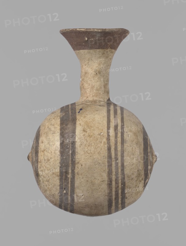 Cypriot gourd jug, A small vessel with a barrel-shaped gourd-shaped body, without a foot, with a spherical bottom. The center is marked with a small protruding point on both short sides. A single handle on the long side, mounted at the greatest bulge of the body and at the base of the neck, bent at a right angle. Quite long neck, strongly flaring, conical spout. Neck and handle slightly offset from the vessel axis; the handle is mounted at a slight angle, with a very clear trace of finger pressure on the right side where it is attached to the neck. Reddish-brown clay. Yellowish-brownish engobe. Decoration in black-brown and matte red. The rim is decorated externally with a wide matte red band. The body is decorated on both sides with two groups of three concentric black-brown lines, of varying widths and spacing. In the groups on the shorter sides, the outer line is much wider than the others. Protruding points are marked in black-brown. Preservation condition: cracked and glued neck a...