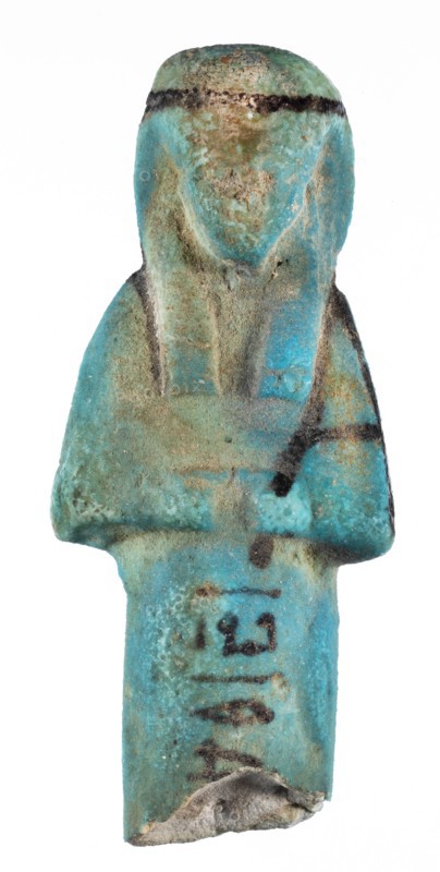 Shabti with baskets on the back, Mummy-shaped funerary figurine, preserved fragment from the knees up. Arms crossed on the chest, hands level next to each other holding hoes. Rectangular basket slung on strings over both shoulders on the back. Long, smooth three-part wig with a headband; triangular face, proportional details, eyes slightly closed; painted facial details and headband. Painted inscription in a column separated by vertical lines on the front of the legs beginning just below the folded hands: ...of the soul belonging to Osiris.... ca. 1069–715 BC, Third Intermediate Period, 21st–23rd Dynasty, Egypt. Shabti, height 7.6 cm, width 3.2 cm., A small sculpted figure photographed against a white background, showing a stylized torso and head with a rounded top and a flattened base; the surface is worn and pitted with a rough texture. The piece displays a turquoise-blue overall color with areas of greenish-blue and pale green patina, along with patches of brownish tan and sandy bei...