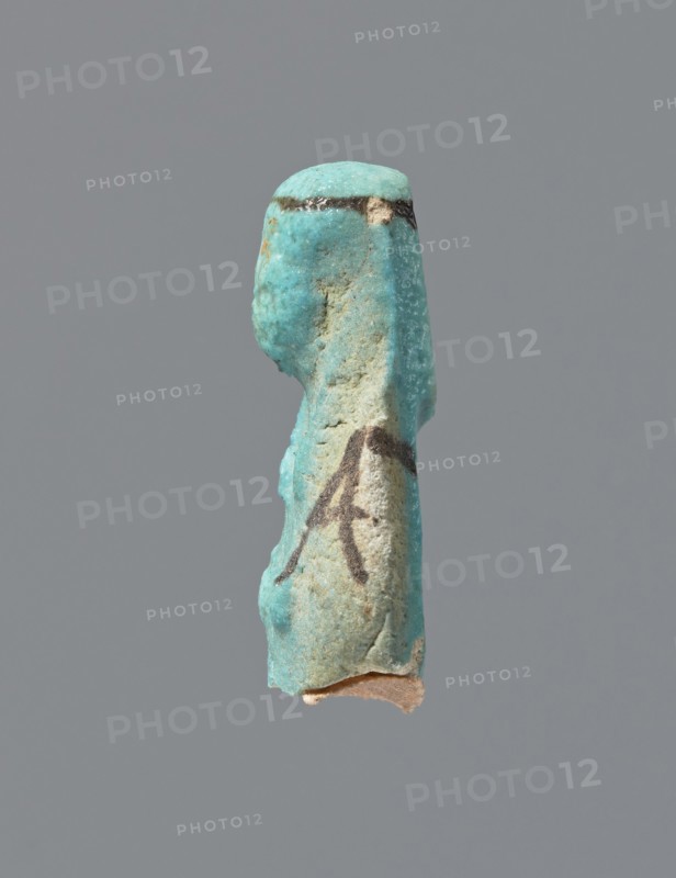 Ushabti, mummy-shaped figurine, preserved head and fragment of torso. Arms crossed on the chest, hands placed at the same level, next to each other, holding hoes in each hand. On the back, a square basket is slung on strings over both shoulders. Wearing a long, smooth, tripartite wig with a headband. Triangular face with details almost illegible. Headband and tools painted. ca. 945–715 BC; Third Intermediate Period, 22nd–23rd Dynasty, Egypt. Ushabti; height 3.7 cm., A small worn figurine fragment shown against a plain gray background, predominantly turquoise in color with areas of pale beige and sandy texture; the piece has a curved head and a vertical, elongated body with rough, weathered surfaces and a few darker brownish marks along the top edge and midsection, and a small exposed beige base at the bottom.