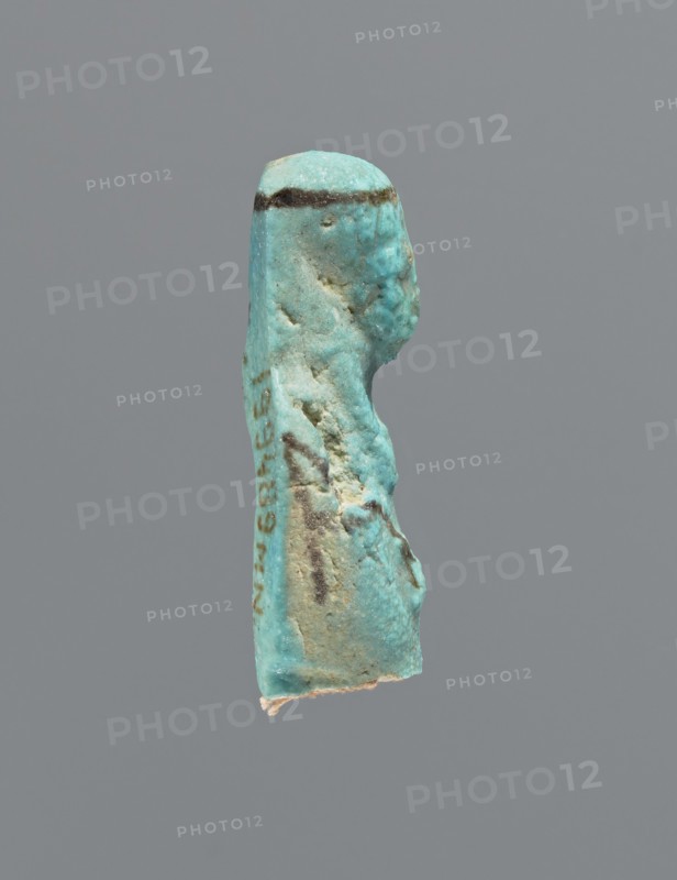 Ushabti, mummy-shaped figurine, preserved head and fragment of torso. Arms crossed on the chest, hands placed at the same level, next to each other, holding hoes in each hand. On the back a square basket is slung on strings over both shoulders. On the head is a long, smooth, tripartite wig with a headband. Triangular face, details almost illegible. Headband and tools painted. ca. 945–ca. 715 BC; Third Intermediate Period, 22nd–23rd Dynasty, Egypt. Ushabti, height 3.7 cm, A small sculpted object in shades of turquoise and aqua with areas of pale beige and darker brownish-green streaks is shown against a plain gray background; the object has an elongated vertical shape with a rounded top and irregular, textured sides, and a slightly rough, uneven surface with a few pits and worn areas; a darker horizontal band runs near the top, and there are several darker spots and streaks along the body, while the lower edge shows a lighter, almost whitish area.