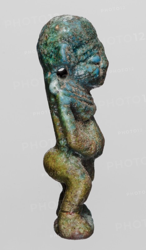 Amulet - Ptah the Dwarf Pataikos, Ptah the Dwarf myth., Egyptian deities, protective amulet, 664–332 BC; Late Period, Egypt, amulet, height 4.5 cm, width 2.2 cm, A small sculpted figure shown in profile with a textured surface displaying shades of blue, green, and brown, with remnants of darker and lighter patina; the figure has a rounded head, a pronounced forehead and nose, a visible ear and an open circular hole near the temple; the torso appears compact with rounded breasts and a slightly protruding belly, arms bent with hands placed near the head, and a narrow back that transitions into thick, bent legs and rounded feet; the surface shows rough, pitted areas and smoother glossy patches, with color variations including turquoise, teal, moss green, olive, rusty brown, and hints of pale blue against a plain light gray background.