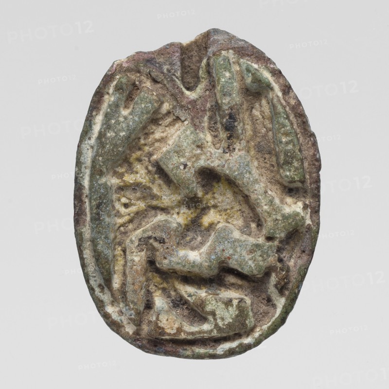 Scaraboid with a monkey. The upper surface is decorated with a convex image of a seated baboon facing right, with the fur on its back marked with crisscrossing lines. On the base is depicted a lying sphinx lion? wearing a feathered crown, above it is a solar disk. In front of the sphinx is the figure of a seated goddess Maat?, above the sphinx's back is visible a lying feather of Maat and possibly another symbol, damaged. c. 1550–c. 1186 BC; New Kingdom, 18th–19th Dynasty, Egypt. Amulet, scaraboid; height 2.3 cm, width 1.7 cm., An oval, weathered object with an uneven, carved surface showing raised and recessed shapes; the surface displays a mix of green, brown, gray, beige, and pale yellow tones with patches of darker brown and small areas of lighter off-white; the edges are worn and irregular, and the overall texture appears rough and pitted with layered ridges and rounded indentations suggesting erosion or age.