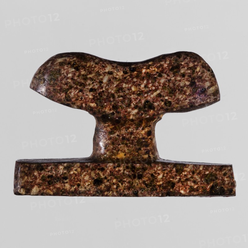 Amulet - headboard, furniture protective amulet in the shape of a miniature headboard; Late Period, Egypt, 664–332 BC; amulet; height 2.8 cm, width 1.8 cm, A small T-shaped object with a speckled surface in shades of brown, reddish-brown, dark green, and pale beige, with a smooth glossy texture and subtle highlights; the top section is rounded and slightly curved, the central stem is narrower and connects to a flat rectangular base, and the background is a uniform light gray.