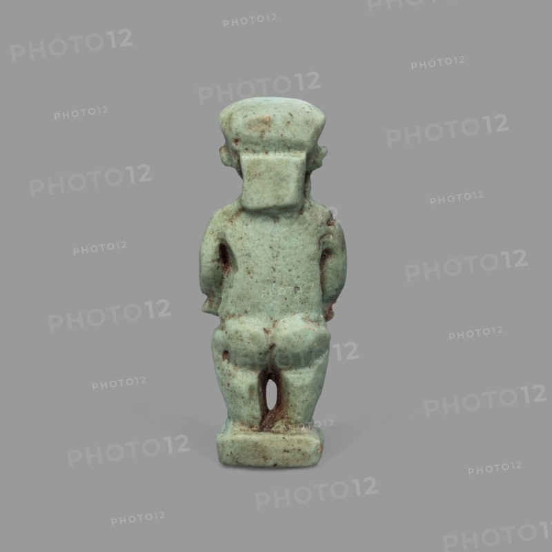 Amulet - Ptah the Dwarf Pataikos, Ptah the Dwarf myth., Egyptian deities, Egyptian religion, amulets. Amulet depicting Ptah the Dwarf Pataikos as a naked, dwarfish man standing with legs slightly apart, hands placed on his sides. Figure on a rectangular base with a hole for hanging behind the neck. 664–332 BC; Late Period, Egypt. Amulet; height 4.3 cm, width 1.7 cm., A small statuette viewed from the back, carved in a pale bluish-green material with areas of darker green and brown discoloration; the figure has a blocky head with a squared rear extension, short arms hanging at the sides, a rounded back and buttocks, and short legs standing on a rectangular base; the surface shows speckled spots and patches of brownish weathering against the predominant bluish-green, and the background is a uniform medium gray.