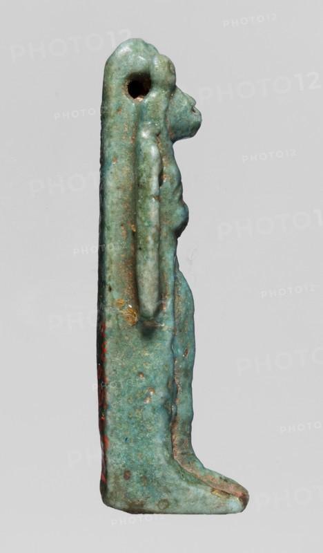 Amulet — figurine of a lion-headed goddess; lionesses; Egyptian deities; Sekhmet, Wadjit, Bastet ; lion-headed goddess with a lotus scepter in her left hand right lowered; 664–332 BC, Late Period, Egypt; amulet; height 4 cm, width 1 cm, depth 1.2 cm., A slender vertical figurine viewed in profile against a pale gray background, showing a stylized human-like form with an elongated head and a rounded back, made of a weathered turquoise-green material with areas of darker green and brownish patina; a hole is visible near the top of the head, a long raised ridge runs down the back, and a slightly projecting chest and stomach are visible along the front; there are a few small spots of reddish discoloration and traces of lighter wear on edges, with subtle variations in texture and mottling across the surface.