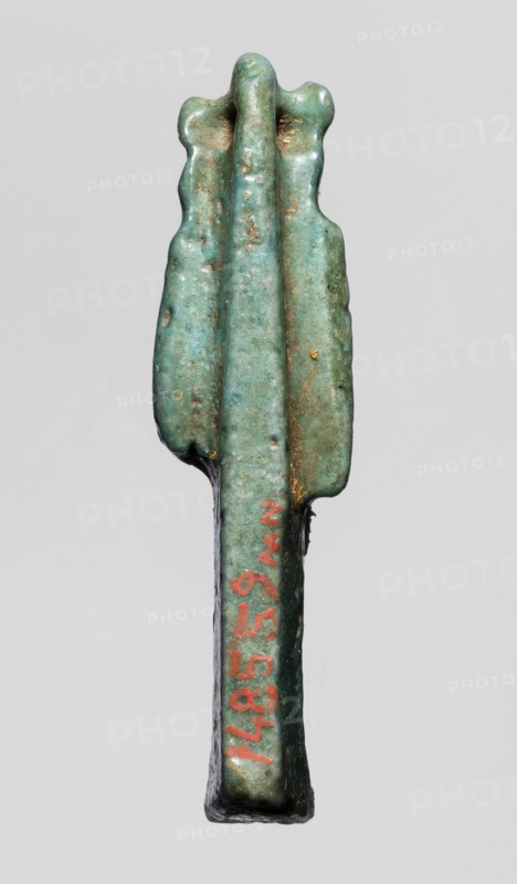 Amulet — figurine of a lion-headed goddess, lionesses, Egyptian deities; Sekhmet, Wadjit, Bastet ; lion-headed goddess with a lotus scepter in her left hand right lowered. 664–332 BC, Late Period, Egypt. Amulet; height 4 cm, width 1 cm, depth 1.2 cm., A small elongated object with a rounded top that has a lobed edge and three raised central ridges, showing a weathered surface in shades of green and turquoise with areas of brownish discoloration and small patches of darker green; the lower portion narrows into a straight stem with a darker underside and a small area of red pigment on one side; the background is a uniform light gray.