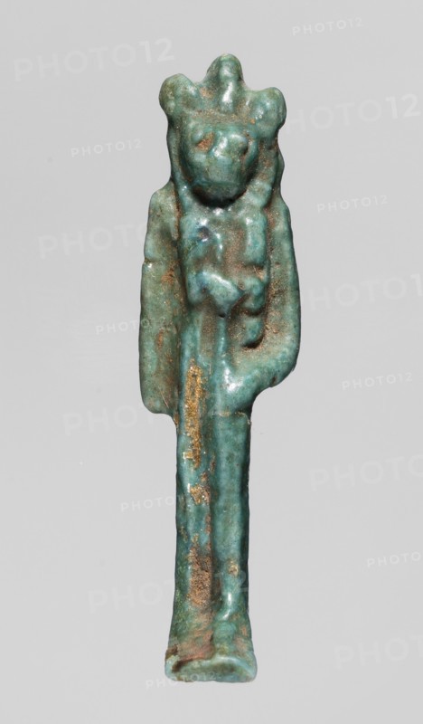 Amulet - figurine of a lion-headed goddess, lionesses, Egyptian deities, Sekhmet myth., Wadjit myth., Bastet myth., Lion-headed goddess with a lotus scepter in her left hand right lowered. 664–332 BC; Late Period, Egypt. Amulet; height 4 cm, width 1 cm, depth 1.2 cm., A small sculptural figure in green-blue and turquoise tones with areas of brownish and goldish discoloration, showing a stylized upright body with an elongated lower portion and a broader upper section that suggests shoulders and a head with rounded protrusions, smooth worn surfaces, subtle raised forms on the torso, and irregular patches of darker and lighter green-blue across the piece.