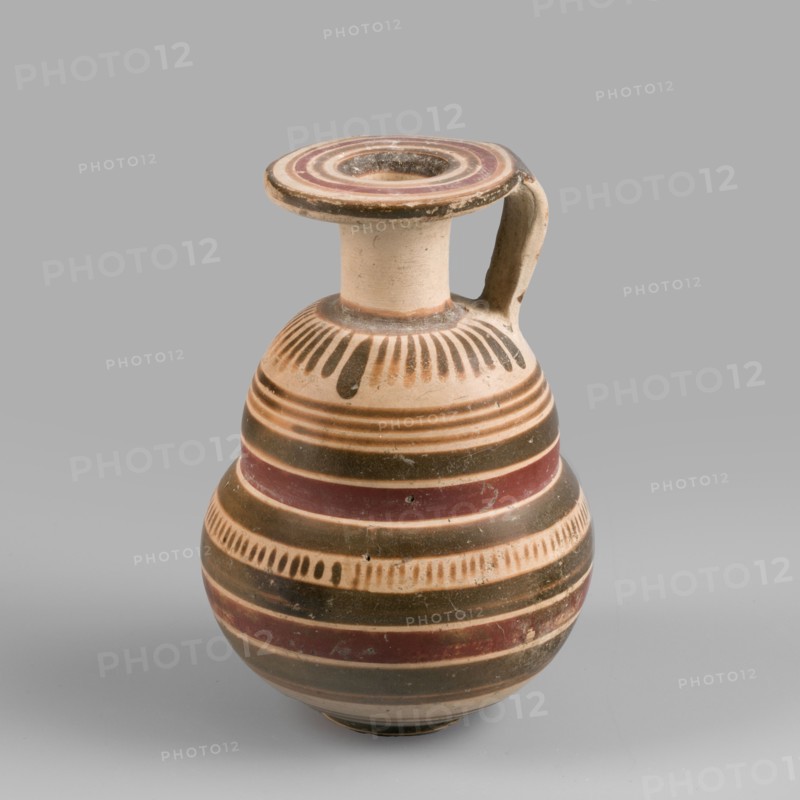Italo-Corinthian aryballos, geometric motifs, Etruscan pottery, 600–575 BC, Etruria, aryballos vessel, weight 0.054 kg, height 7.7 cm, diameter 5.3 cm, An earthenware jug with a rounded body, narrow neck, flat circular rim, and a single curved handle is shown against a plain gray background; the jug displays bands and decorative motifs in beige, dark brown, reddish-brown, and black, with a pattern of vertical brushlike strokes near the shoulder, alternating horizontal stripes around the body, and some worn spots and surface irregularities on the painted finish.