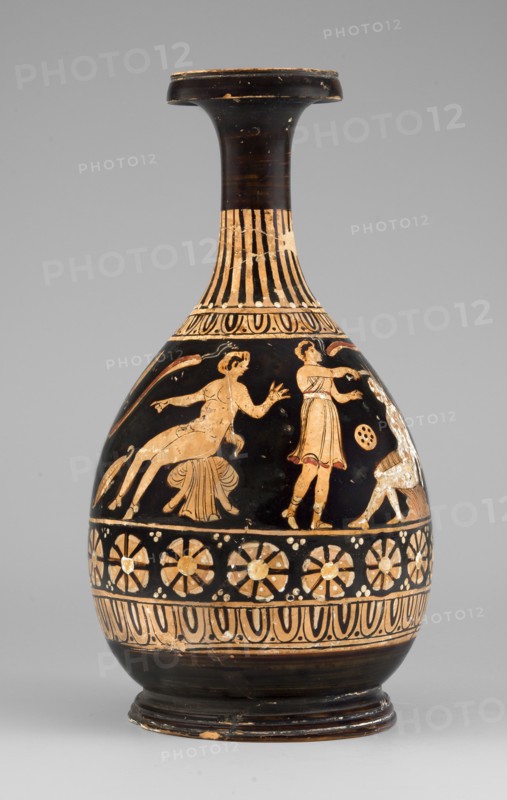 Red-figure bottle with a scene of the punishment of Marsyas, 330–310 BC. Greek pottery bottle height 26 cm, width 13.5 cm, weight 0.67 kg. Vessel glued from several fragments; minor additions on the neck, flaking of white and yellow retouches covering the silhouette of Silenus. Between the ornamental bands covering the lower half of the neck and belly, a scene depicts the punishment of Marsyas. Marsyas sits on the fold of a cloak, the other end covering his right thigh; the lower part of his torso faces left while the upper part, with his hands tied to a tree in front, faces right toward Apollo. Apollo stands next to a table placed on a platform, holding a lyre on it and a taenia in his right hand, which flutters above Silenus’s head. A Scythian stands before Marsyas, holding a knife in his right hand and beginning to flay him. The scene is complemented by three satyrs and a column with an oval object possibly an omphalos. Subject relates to the musical agon between Apollo lyre and Mar...