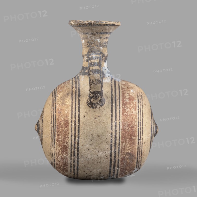Barrel-shaped jug, unknown Cypriot workshop, ca. 850–600 BC, Cyprus Arsinoe.; vessel, height 12 cm, width 10 cm. Barrel-shaped body terminated on both sides by small protrusions. Cylindrical neck terminates in a cup-shaped spout. A band-shaped vise connects the body to the neck midway up. Decoration in brown paint: concentric bands encircling the barrel; two wide light-brown bands on either side of the vise framed by narrow dark-brown bands. At the protrusions the bands form concentric circles. Transverse bands between two vertical bands decorate the vise. A series of concentric belts on the neck. Geometric motifs; Cypriot ceramics., A rounded ceramic vessel with a narrow neck and flared rim sits against a plain gray background; the vessel shows a weathered surface with bands of paint in beige, brown, black, and faded red arranged vertically and symmetrically around the body, and a short vertical handle extending from the neck to the shoulder with striped black and beige markings; the ...