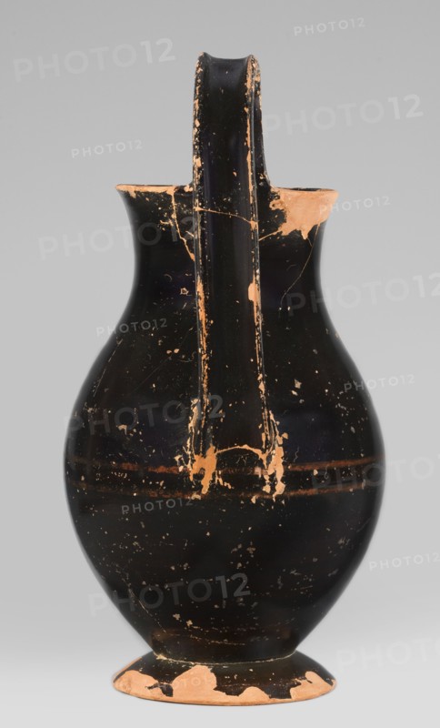 Olpe type of jug for liquids with inscription, unknown Attic workshop; Crito ca. 550–500 BC signature. Black-finished olpe with a clay-coloured cartouche at the point of maximum diameter bearing Crito's signature KRITONEPOIESEN, also reading LEPOSYS. Medium-sized olpe, rim edge slightly turned outwards; low neck gently transitioning into a concave, spherical belly, clearly distinguishable from the low conical foot with a recess. Bottom slightly convex. Profiled vise shaped with clearly distinguishable edges. On the inner side of the rim, two clay nodules one reconstructed are visible, located 4.5 cm apart on the side of the vise. 550–500 BC; Attica, Athens. Olpe vessel. Height 26 cm; width 13.5 cm; depth 15.5 cm; weight 0.58 kg., A single ceramic jug with a rounded body, narrow neck, and a tall handle rising from the rim to the shoulder, shown against a plain light gray background; the jug has a predominantly black surface with worn areas revealing a terracotta color, including chips a...