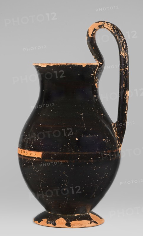 Olpe type of jug for liquids with inscription, unknown Attic workshop; Crito ca. 550–500 BC signature KRITONEPOIESEN, Greek ceramics, pottery marks, Greek inscriptions. Black-finished olpe with a clay-coloured cartouche at the point of maximum diameter inscribed KRITONEPOIESEN. Medium-sized olpe, rim edge slightly turned outwards. Low neck gently transitioning into a concave, spherical belly, clearly distinguishable from the low conical foot with a recess. The bottom of the vessel is slightly convex. The profiled handle vise is shaped with clearly distinguishable edges. On the inner side of the rim two clay nodules one reconstructed are visible, located 4.5 cm apart on the side of the handle. Dating: 550–500 BC. Origin: Attica, Athens. Object type: olpe vessel. Dimensions: height 26 cm, width 13.5 cm, depth 15.5 cm, weight 0.58 kg., A single ceramic jug stands against a plain gray background, showing a rounded body that tapers to a narrower neck with a flared rim and a curved handle ex...