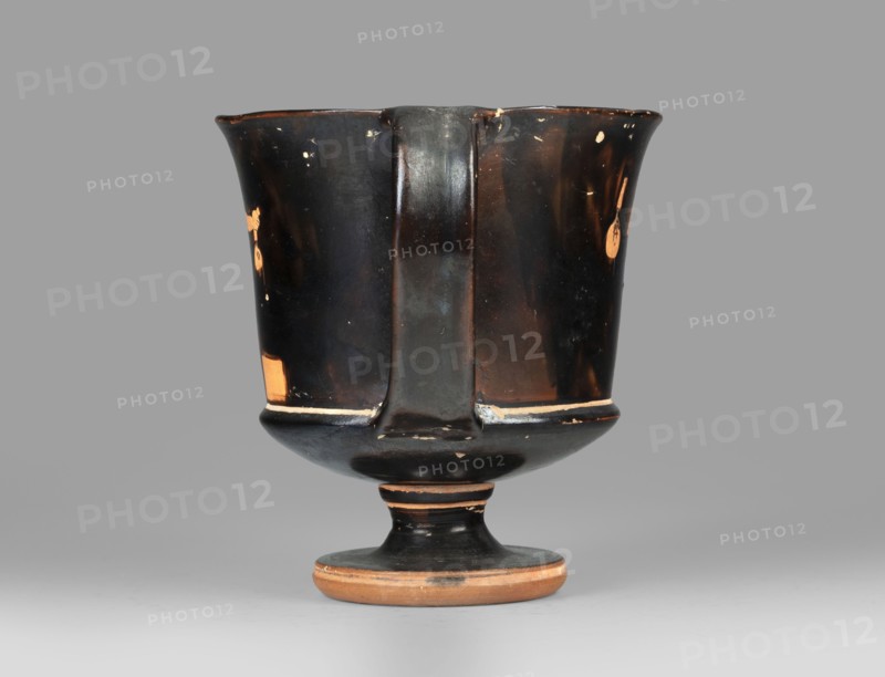Red-figure kantharos with a depiction of an ephebe with an aryballos and a Greek inscription “Beautiful boy”., Kantharos with a slightly flared spout, a deep bowl, a flat bottom, a high profiled stem, a ring-shaped foot. Thin-walled. A: bearded man with a lyre in his head in left profile, holding a lyre in his left hand. B: ephebe with aryballos. The inner surface of the bowl is covered with varnish. Technology: Smooth surface. The varnish is thick, shiny, unevenly fired. Notes: the vessel is intact. Small secondary losses and chips are visible on the surface. Varnish color: 10 YR 2/1 Black. Date: ca. 450 BC mid-5th century BC. Place of origin: Attica. Object type: kantharos vessel. Dimensions: height 11 cm, width 16.2 cm, depth 10.2 cm., A single ceramic cup with a stemmed base sits centered on a neutral gray background; the cup has a flared rim, a straight central handle running down the front, and a rounded foot. The surface is predominantly black with worn areas revealing a warm te...