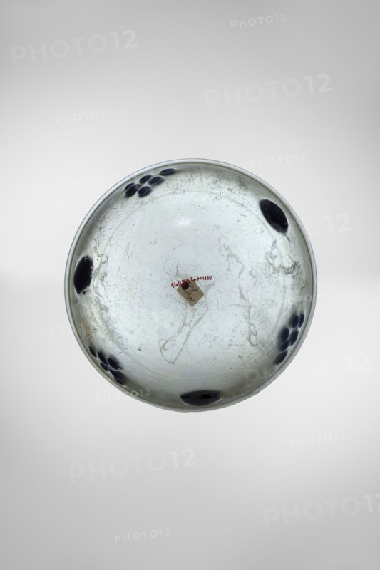 Bowl decorated with knobs, hemispherical bowl or lamp decorated with cobalt oval discs; light green, transparent free-blown glass with decorative translucent cobalt discs placed in one line halfway up the bowl in six places in two alternating arrangements 1 — a single large disc, 2 — six smaller ones arranged like a grape. Isings form 106 96A. Outer diameter of rim 14.30 cm; height 9.30 cm; weight 0.306 kg; 4th century, Syria., A round shallow bowl viewed from above with a pale off-white to light gray interior and subtle darker gray scuff marks and scratches, decorated with a few clusters of dark blue circular spots near the rim and several larger dark blue oval spots spaced around the edge; the rim has a thin slightly darker line and the background is a smooth gradient of light gray to white.