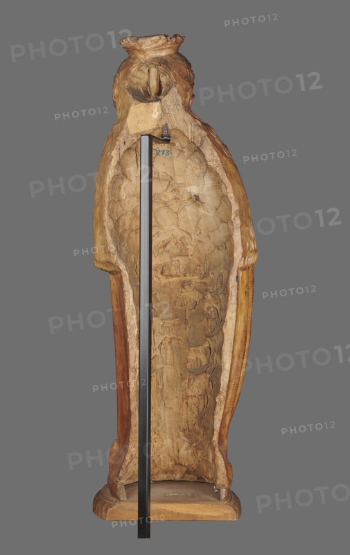 Figure of St. Barbara, St. Barbara d. 306. Medieval wall sculpture, hollowed out from behind the head also has a circular hollow. Depicts St. Barbara in contrapposto, creating a slight S-shaped silhouette. Slightly oversized head on a cylindrical neck; elongated face with high forehead, straight narrow nose, full cheeks, small smiling mouth with dimples and a dimple in the chin. Long hair framing the face and falling down the back, one strand draped over the right shoulder, carved as thin parallel wavy strands. Wears a crown finial broken. Right hand grasps the stem of a chalice, left hand fingers covered by a cloak supports the foot of the chalice. Dress with triangular neckline and long wide sleeves, cinched at the waist with a decorative belt; voluminous cloak with numerous folds formed into dry, thin ridges. Pointed left shoe peeking from beneath folds. Round, irregularly carved base. No polychrome. Ca. 1500, probably Silesia. Sculpture. Height 102.0 cm; width 35.0 cm; depth 24.0 c...