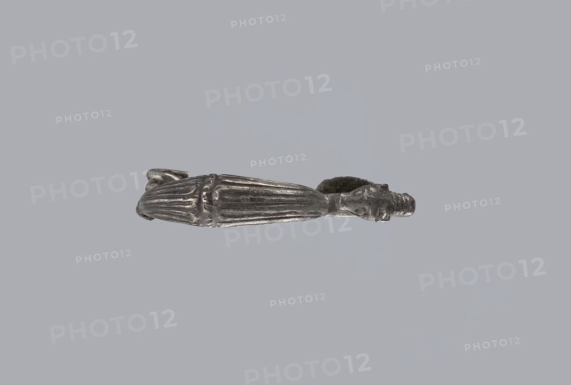 Snake-headed fibula, unknown Southern Italian workshop. Fibula with an arched, thick hoop. The hoop is terminated on one side with an imitation spiral, and on the other side connected to the rectangular wall of the sheath, bent at the bottom. A cylindrical leg extends from the sheath, bent towards the hoop, ending with a snake's head. The hoop is decorated with numerous longitudinally engraved lines. Condition: corrosion, missing needle. 5th–4th century BC, Southern Italy. Materials: silver. Iconography: snake., A metallic object with a silver-gray finish is shown against a pale gray background; it appears elongated with a tapered central section featuring raised ridges and fluting, a rounded end with a small protrusion, and a ring-like opening at the opposite end that has an irregular, textured surface; the metal shows darker gray shadows and lighter silver highlights across its surface.