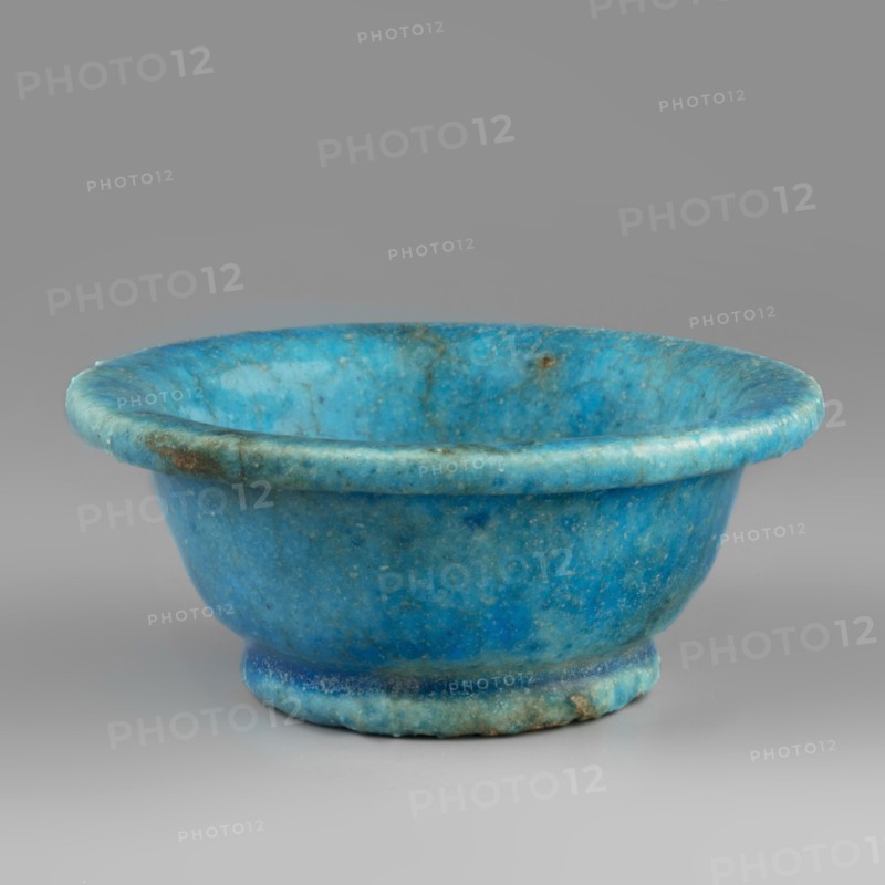 Bowl, Goluchów Greater Poland Voivodeship, faience vessel, bowl with a slightly rolled-up rim on a ring-shaped foot, made of faience covered with a blue glaze. 332–30 BC; Ptolemaic Period, Egypt. Vessel; height 4 cm, width 10 cm., A shallow rounded bowl with a rolled rim and a short foot, made of a mottled blue material showing variations from bright turquoise to deeper cyan with areas of greenish and darker blue veining and some small brownish spots and mottling, set against a neutral grey background.