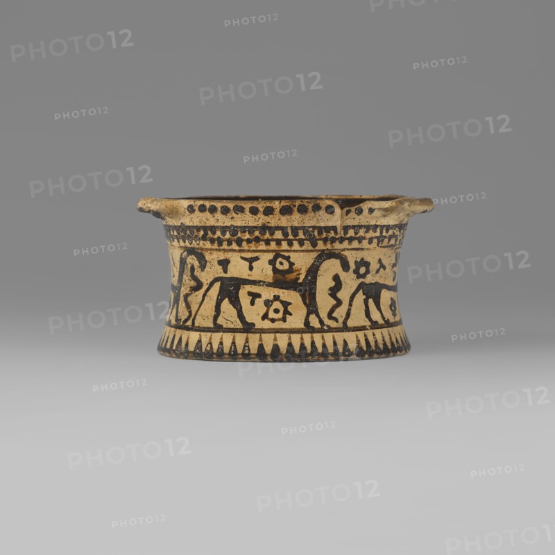 Orientalising pyxis with an animal frieze in the Silhouette style, Images of animals; Middle Corinthian period, cats. Thin-walled pyxis with a straight rim, slightly concave body walls, and a flat bottom. Small vices mounted horizontally just near the edge of the rim. The main decorative band, bounded at the top and bottom by a thin line of varnish, depicts figures of animals executed using the silhouette technique. Between the silhouettes there are simplified filling ornaments. Clay color: 5 Y 8/2 pale yellow Varnish color: 5 Y 2.5/1 black Dating: 590–570 BC Middle Corinthian period. Place of origin: Corinth. Object type: pyxis vessel. Dimensions: height 5.3 cm, width 10.2 cm, depth 8.5 cm, weight 0.102 kg., A shallow, cylindrical ceramic vessel sits centered against a gray background, showing a beige base color with black painted decoration; the body flares slightly at the rim which has a couple of small protruding tabs, and the rim edge and interior top band are marked by rows of bl...