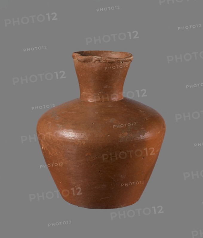 Jug, ceramics, Egyptian pottery. Medium-sized clay jug with a biconical body, widest at about half its height; wide shoulders; wide, almost cylindrical neck widening toward the spout neck about one-third of total height. Profiled, irregular spout, slightly raised and extended on one side forming a small spout; spout nearly triangular in cross-section with a ~1 mm cylindrical bulge on the outer profile. Bottom almost flat, very slightly rounded. Made of Nile clay NB1?; neck likely made separately and attached to the shoulders. Outer surface leveled, covered with engobe and polished; inner surface leveled except for neck, which is also engobed and polished. Color reddish-brown. Well preserved; rim slightly chipped in two places and engobe worn in places on outer surface. Dated to the 6th Dynasty; origin Edfu. Dimensions of a comparable type: height 20.5 cm, rim diameter 8.5 cm, body diameter 17.3 cm, bottom diameter 10.9 cm. Analogous example in the Louvre E 16586. References: Reisner, M...