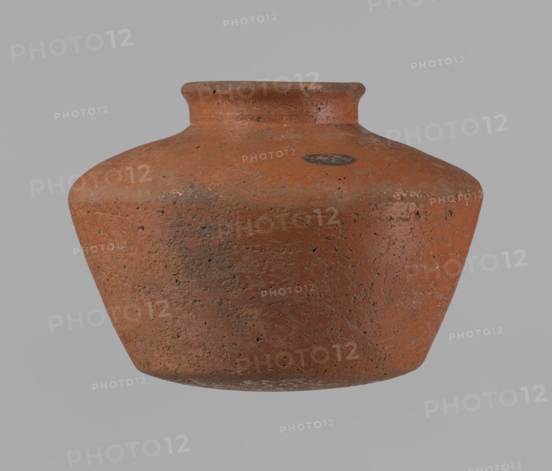 Vessel, Egyptian pottery vessel ceramic, clay, c. 2686–c. 2181 BC, Old Kingdom; excavated at Edfu. Vessel: height 11 cm; rim diameter 6.3 cm; body diameter 14.7 cm; bottom diameter 10 cm., A single rounded clay pot with a short neck and flared rim sits against a plain background; the pot has a rough, pitted surface texture with visible irregularities and wear, showing a primary reddish-brown color with areas of darker brown and small patches of lighter, almost pinkish tones, along with a few darker grayish spots and some subtle white residue near the base.