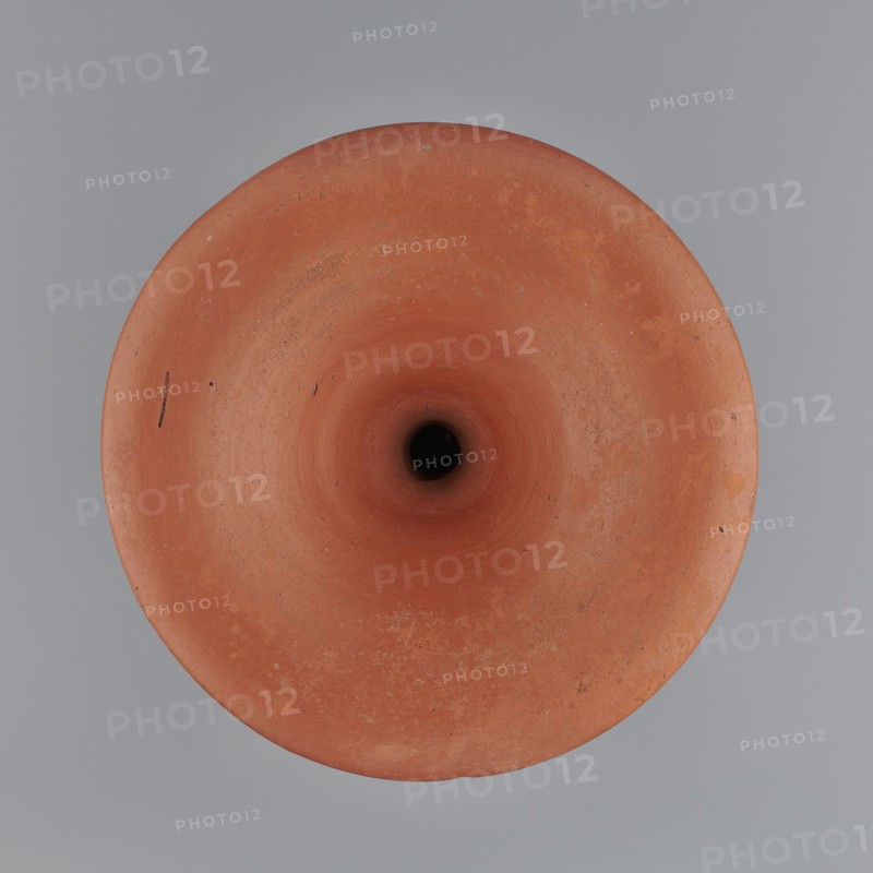 Bowl base. Base for a vessel with an almost equal diameter of both rims; both rims are irregular with a wavy line. The center of the base is empty. The narrowest part of the base is approximately 2/3 of the height of the entire vessel. Vessel made of Nile clay NB1. Surface leveled and covered with an engobe, then polished. Vessel color: red. Complete vessel, very well preserved. c. 2494–c. 2181 BC; Old Kingdom, 5th–6th Dynasty, Edfu. Vessel; top diameter 17.5 cm, bottom diameter 18 cm, height 25.6 cm, weight 1.30 kg., A top-down view of a round terracotta object with a central dark hole, showing a smooth funnel-like interior and rim with some surface speckles and small imperfections, set against a smooth gray background; the visible colors are reddish-brown, dark brown to black in the center, and gray.