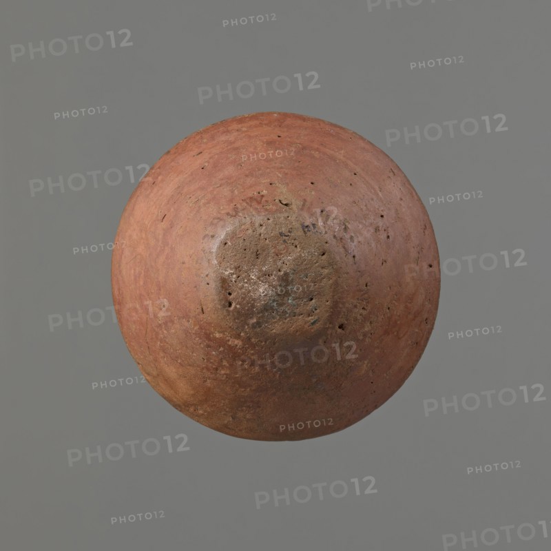 Vessel, Egyptian pottery vessel of clay, c. 1650–c. 1550 BC Second Intermediate Period, Edfu. Height 7.4 cm; rim diameter 5.5 cm; belly diameter 8.2 cm., A round, weathered object with a rough, pitted surface floating against a plain background, showing a predominately reddish-brown color with areas of muted orange, rusty brown, and small patches of darker brown and gray; the surface texture includes irregular marks, small holes, and uneven discoloration, and the background is a solid gray.