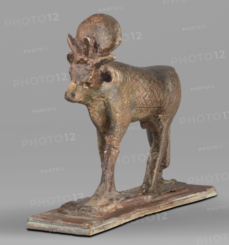 Apis bull figurine, Apis mythology, bulls, Scen.Gal.Eg., sacred animals, animal figurines, Egyptian art, Sacred animal of the god Ptah, 664–525 BC; Late Period, 26th Dynasty, Egypt, figurine, height 7 cm, width 6 cm, weight 0.164 kg, A small metallic sculpture of an animal stands on a rectangular base, showing a textured body and slender legs. The figure has a rounded head with a pair of upright ear-like projections and a raised circular shape atop the head, along with a short snout and visible facial contours. The surface shows uneven texture and carved crosshatch patterning on the torso. The base is flat and slightly raised with worn edges. Visible colors include brown, bronze, gold, greenish patina, and hints of gray.