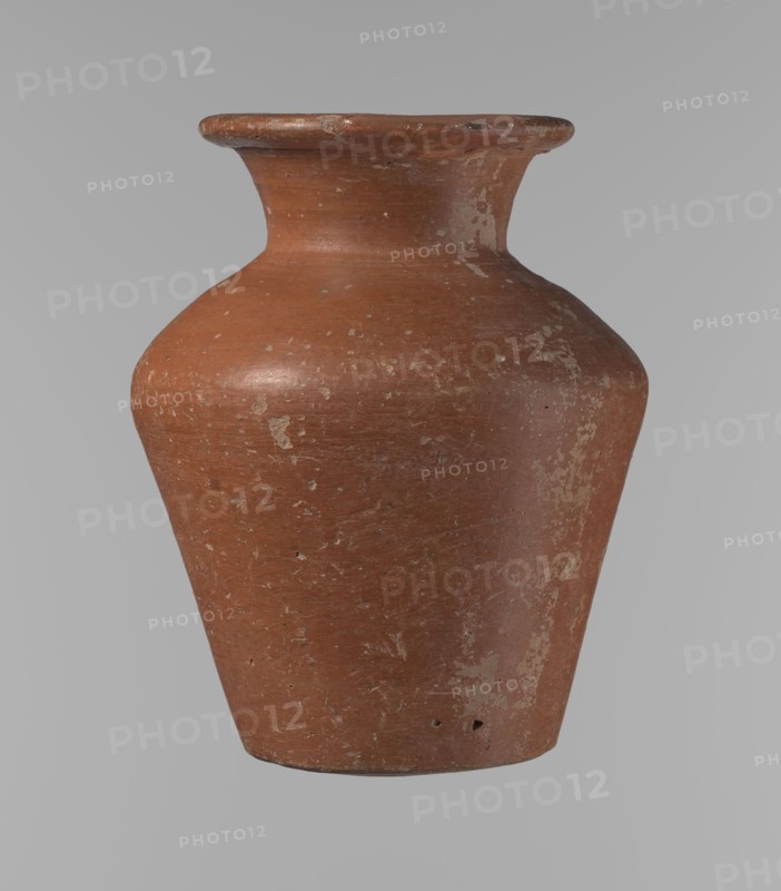 Vessel, Egyptian pottery ceramic clay vessel, conical, widest at approximately 3/4 of its height. Shoulders wide, almost horizontal, slightly sloping. Neck wide, short, funnel-shaped, widening towards the spout. Spout wide, flat in the upper part, slightly rounded at the bottom, slightly asymmetrical. Bottom slightly convex, asymmetrical. Surface even. Lower part worked to approximately 2/3 of its height with a knife or similar tool. Outer surface and inner surface of rim and neck covered with a layer of dark red engobe. Color dark red. Vessel complete; surface eroded in many places, numerous clay chips on the rim. Old Kingdom, ca. 2686–2181 BC; provenance: Edfu. Height 16.7 cm; rim diameter 9.5 cm; body diameter 13 cm; bottom diameter 8.1 cm. References: Reisner, Mycerinus, p. 219, types XIX and XX, fig. 69., A single terracotta-colored ceramic vessel with a rounded shoulder, flared rim, and tapered base, showing areas of worn and chipped surface with lighter beige and off-white patch...