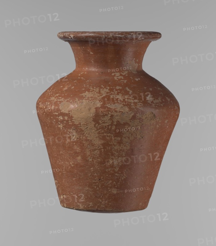 Vessel, Egyptian pottery, clay vessel; conical shape, widest at approximately 3/4 of its height. Shoulders wide and almost horizontal, slightly sloping. Neck wide, short, funnel-shaped, widening toward the spout. Spout wide, flat in the upper part, slightly rounded at the bottom, slightly asymmetrical. Bottom slightly convex, asymmetrical. Surface even. Lower part worked to approximately 2/3 of its height with a knife or similar tool. Outer surface and inner surface of rim and neck covered with a layer of dark red engobe. Vessel color dark red. Vessel complete; surface eroded in many places with numerous clay chips on the rim. Attributed to ca. 2686–2181 BC, Old Kingdom, Edfu. Height 16.7 cm; rim diameter 9.5 cm; body diameter 13 cm; bottom diameter 8.1 cm. References: Reisner, Mycerinus, p. 219, types XIX and XX, fig. 69., A single aged ceramic vase with a wide flared rim and a rounded shoulder tapering to a narrower base is shown against a plain neutral background. The surface of the...