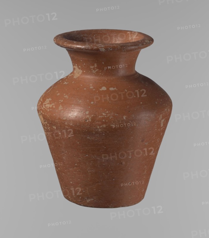 Vessel, Egyptian pottery, clay vessel: a conical vessel, widest at approximately 3/4 of its height. Shoulders quite wide, almost horizontal—slightly sloping. Wide, short, funnel-shaped neck widening towards the spout. Spout wide, flat in the upper part, slightly rounded at the bottom, slightly asymmetrical. Bottom slightly convex, asymmetrical. Surface even. Lower part worked to approximately 2/3 of its height with a knife or similar tool. Outer surface and inner surface of rim and neck covered with a layer of dark red engobe. Vessel color dark red. Vessel complete; surface eroded in many places, numerous clay chips on the rim. Ca. 2686–ca. 2181 BC; Old Kingdom, Edfu. Vessel height 16.7 cm; rim diameter 9.5 cm; body diameter 13 cm; bottom diameter 8.1 cm. References: Reisner, Mycerinus, p. 219, types XIX and XX, fig. 69., A single rounded ceramic vessel with a flared rim and narrow neck sits against a plain background; the surface shows worn patches and speckled areas with a textured, ...