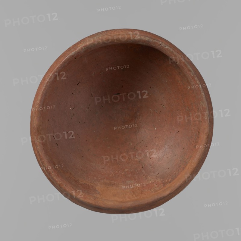 Medum-type bowl, A small Medum-type bowl with characteristic carination under the rim. Rounded bottom. Arched walls, gently breaking towards the center of the vessel around 2/3 of its height. Straight, perpendicular rim. Narrow, sloping shoulders. The diameter of the rim is significantly smaller than the diameter of the vessel's arms. Clay probably NB2. The vessel's surface is leveled and covered with a layer of engobe, and then polished. Vessel color - red. c. 2686–2181 BC; Old Kingdom, Edfu. Vessel; height 4.5 cm, diameter 11 cm rim, diameter 11.6 cm arms., A top-down view of a round, shallow bowl with a smooth continuous rim, showing an interior surface with a worn, slightly uneven texture and tiny pits and scratches. The bowl is primarily reddish-brown with areas of darker and lighter brown, and subtle hints of ochre and grayish tones along the rim and inner curve. The background is a flat neutral gray.
