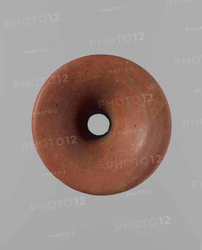 Bowl stand, unknown creator. Base for a vessel with an almost equal diameter of both rims. Both rims are irregular, with a slightly wavy line. The center of the base is empty. The narrowest part of the base is approximately 2/3 of the height of the entire vessel. Made of Nile clay NB2. Surface leveled, covered with an engobe, then polished. Vessel color: red. Complete, very well preserved. Set with bowl. Ca. 2494–ca. 2181 BC; Old Kingdom, 5th–6th Dynasty, Edfu. Vessel; height 13.7 cm; diameter 10.2 cm rim; diameter 9.3 cm bottom., A top-down view of a round, hollow object with a smooth, concave interior and a central circular opening, showing a worn terracotta surface with small pits and irregularities in shades of reddish-brown and darker brown, set against a plain light gray background.