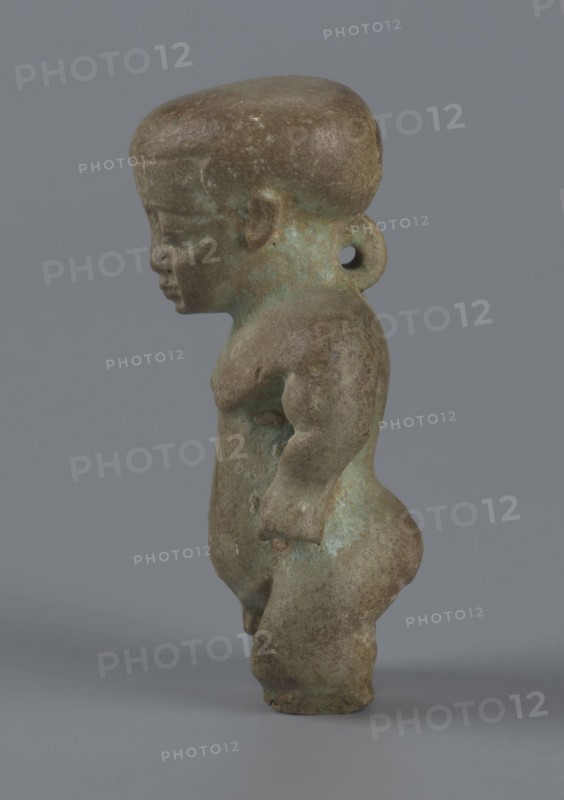 Amulet - Ptah-dwarf Pataikos, Ptah-dwarf mythology. Figurine of a naked dwarf man with a large head with a wide forehead, short arms with clenched fists pressed to the hips, and short legs broken off at the knees. Careful modelling. 7th–4th century BC; Late Period, Egypt. Figurine, amulet. Height 6.5 cm; width 3.7 cm; depth 2.6 cm., A small sculpted figure viewed in profile against a plain gray background, showing a stylized human form with a rounded head, pronounced forehead, and a short neck with a circular loop at the back. The figure has a compact torso, rounded shoulders, a slightly protruding chest, and short arms with simplified hands resting near the hips. The lower body features full hips and sturdy legs with rounded knees and feet. The surface appears weathered with mottled tones of brown and greenish-blue patina, with some areas darker brown and others showing lighter greenish corrosion. The overall texture looks rough and aged.