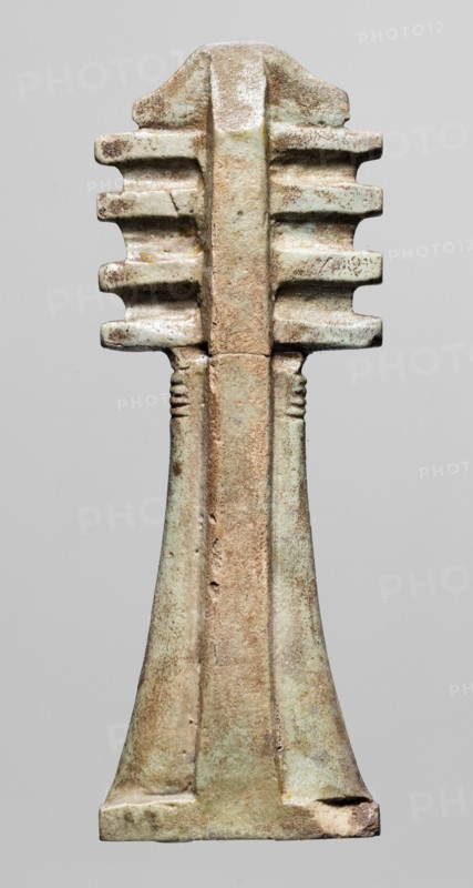 Amulet — djed pillar. Amulet in the shape of the djed hieroglyph with a pillar at the back; at the top a trapezoidal projection decorated with vertical striations and below four crossbars; the top of the shaft has horizontal incisions. Material: amulet; period: Late Period, Egypt, 664–332 BC. Dimensions: height 9 cm, width 3.3 cm., A vertical carved object with a symmetrical form, showing a textured surface in shades of pale green, light brown, beige, and hints of darker brown; the top has a rounded central ridge with tiered horizontal protrusions on both sides that create a stacked, ribbed appearance; the middle narrows into a slender, slightly raised central column with subtle linear grooves near its upper portion; the lower section flares outward into a trapezoidal base with worn and rough edges, exhibiting variations in patina and small surface pits and scratches.