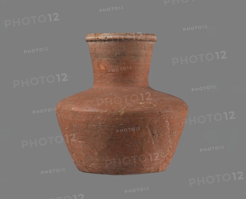 Jug, Small handleless jug with a biconical body, widest at about half its height; broad, rather flat shoulders. Neck wide, almost cylindrical, widening slightly toward a profiled, irregular spout that slopes down on one side and extends to form a small beak; spout cross-section triangular with an approx. 1 mm central indentation on the outer profile. Neck was formed separately and attached to the shoulders. Bottom almost flat, very slightly rounded. Made of Nile clay NB1/2? Vienna System. Outer surface and inner surface of rim and neck smoothed and covered with an engobe; remaining inner surface leveled. Red-brown color. Almost complete—small rim fragment missing; outer surface slightly worn in places. Old Kingdom, possibly 4th–6th Dynasty; provenance: Edfu. Vessel; height 11.4 cm; diameters: rim 5.5 cm, shoulders 10.8 cm, bottom 7.1 cm., A single rounded clay vessel with a narrow neck and flared rim sits against a plain background; the vessel has an uneven, slightly rough surface with...