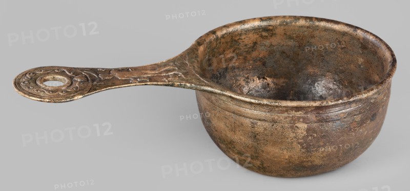 A ladle with a handle decorated with a depiction of Mercury, Mercury myth., Roman deities, ladles, 1st century, Roman Empire 27 BC–476, vessel; height 6.5 cm, width 25 cm, depth 13.5 cm, weight 0.62 kg, A metal ladle with a rounded bowl and an elongated handle is shown against a neutral light gray background; the object displays a worn, mottled surface with a mix of brown, bronze, dark brown, greenish patina, and hints of black, and the interior and exterior of the bowl show textured pitting and discoloration; the handle features a decorative circular end with raised swirling motifs and a central hole, and the handle surface shares the same aged, speckled coloration as the bowl.