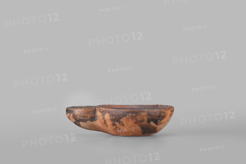 Lamp decorated with a depiction of a dog, unknown eastern workshop; single-burner oil lamp, 1st century, Roman Empire 27 BC–476; dogs iconography; weight 0.082 kg., A low, rounded object with an irregular, boat-like shape sits on a flat surface; its surface shows a mottled pattern of brown, dark brown, and black tones with patches of lighter brown and small speckled areas, and the top has a shallow recessed area while the sides curve smoothly and show wear and texture.