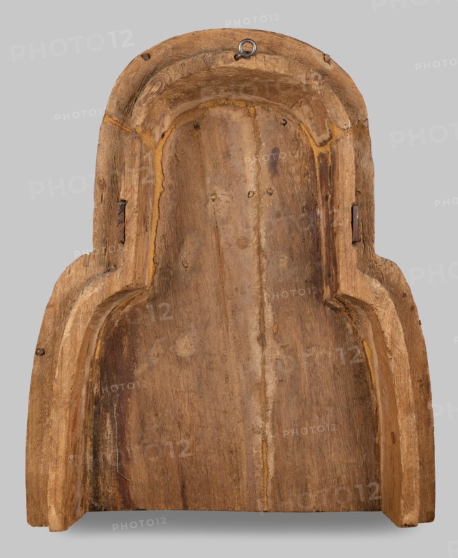 Fragment of a sarcophagus lid. Part of the lid of an anthropoid woman's sarcophagus. Large, striped wig falling on the breasts at the front, decorated with four diadems of lotus petals and vulture wings, and bands of rosettes at the ends. On the breast is a multi-row necklace, with lotus flowers and rosettes forming the lower row. Lotuses, vulture vulture wings, element of the so-called vulture diadem, necklace, wigs, funerary equipment, lotus flower decorative motif. Egyptian art. c. 945–c. 735 BC; Third Intermediate Period, 22nd Dynasty, Egypt. Sarcophagus. Height 62 cm, width 49 cm, depth 20 cm., A carved wooden object with a rounded top and stepped sides, showing a worn, rough surface and visible grain; the wood varies in shades of brown with lighter tan highlights along edges and recessed grooves, and a few darker brown streaks and patches; there is a small metal hanging loop near the top center showing a gray-silver color; the background is a flat light gray.