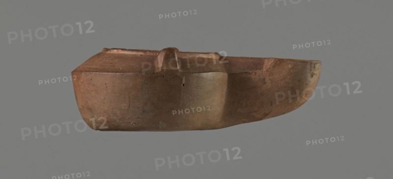 Lamp with a tragic mask, unknown Italian workshop. Oil lamp, single-burner, Roman, Buchi type IX-b = Loeschcke type IXb. Lamp from a mold. Round vessel with arms drooping to the outer, separated from the disc by a convex edge. Two bars arranged symmetrically on the arms. Concave, flat disc with two olive holes located on either side of the convex representation in the form of a theatrical tragic mask. Medium-length wick channel, decorated with a groove in the center and a small air ventilation hole in the center of the groove. Rounded end of the burner. Slight trace of use dark discoloration near the wick hole. On the bottom, a convex inscription workshop trademark: COMMUNIS. Compare with MNW 236765, second half of the 1st/beginning of the 2nd century, Modena. Dimensions: height 9 cm, width 4.4 cm, depth 3.3 cm., A brownish clay object with a smooth, rounded body and a flattened top, showing a few subtle surface imperfections and small pits, set against a neutral gray background; the o...