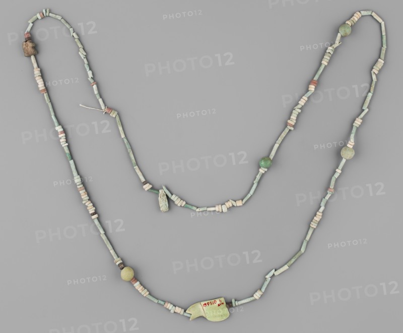 Necklace, repossession Radom. Egyptian deities, udjat eyes, beads, spherical beads, ornaments. Necklace consisting of 67 straw-shaped beads, 117 flat rings, 10 double flat rings with two holes, 4 balls, 2 udjat eyes 1 eyelet in 2 parts, 1 deity figurine without preserved feet. Predominant color: green; single beads brick-red, brown, and white. 664–332 BC, Late Period, Egypt. Amulet, jewelry; height 98 cm., A beaded necklace arranged on a flat gray background, composed of a string of small cylindrical and disc-shaped beads in pale green and off-white, with several beads in muted pink and some round beads in green and yellowish tones; a larger pale green pendant with an irregular shape is attached near the lower center, and there are a few small rough stone or clay beads in beige and brown along the strand.