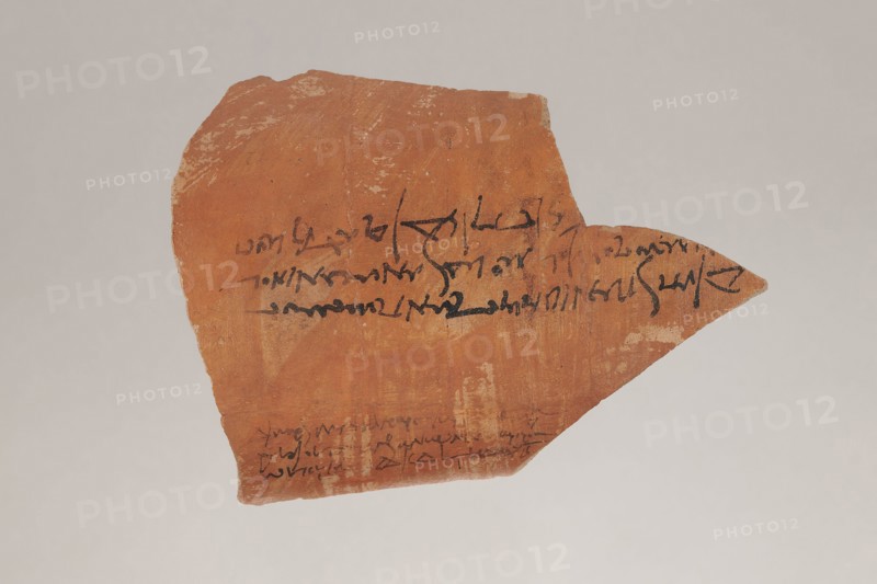 Greek ostraka – two tax receipts, unknown creator/author, taxes, receipts. Fragment of a clay vessel with two tax receipts paid by Panibekis, son of Achillas Rufus, 27/04/161, Edfu Apollonopolis Wielka. Ostraka; height 11.5 cm, width 15.5 cm, depth 0.5 cm, weight 0.136 kg., A broken, irregularly shaped shard with a warm reddish-brown surface sits against a light gray background, showing areas of lighter beige where the surface is worn; a few strokes of dark black markings appear across the shard, and there is a slender pointed extension on one side; the shard's texture looks rough and slightly pitted with subtle variations of red, brown, beige, and tan.