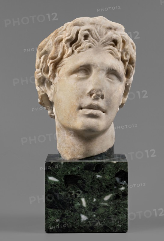 Head of Alexander the Great, unknown Roman workshop. Alexander III the Great King of Macedonia; 356–323 BC. Male portrait, Roman sculpture, Roman copy from a Greek original; head. The head of a young man is clearly turned to the left in a pathetic manner. The head is reflected at the base of the neck. The face is oval, the skeletal structure is not emphasized. The mouth is prominent, with slightly parted lips. The nose is straight, reflected at the tip. The eyes are almond-shaped, deep-set, and the eyebrows are expressive, protruding strongly above the eyeball. The forehead is flat, low, and covered with lush locks of hair. The hairstyle consists of loosely arranged, slightly curled locks. Above the forehead, shifted off-axis to the right, a lock of hair is visible, radiating outwards, slightly raised and clearly different from the other locks. At the back of the head, the hair is arranged in wavy locks, with only the lower part being freely arranged. Date: 140–160 AD formerly dated 15...