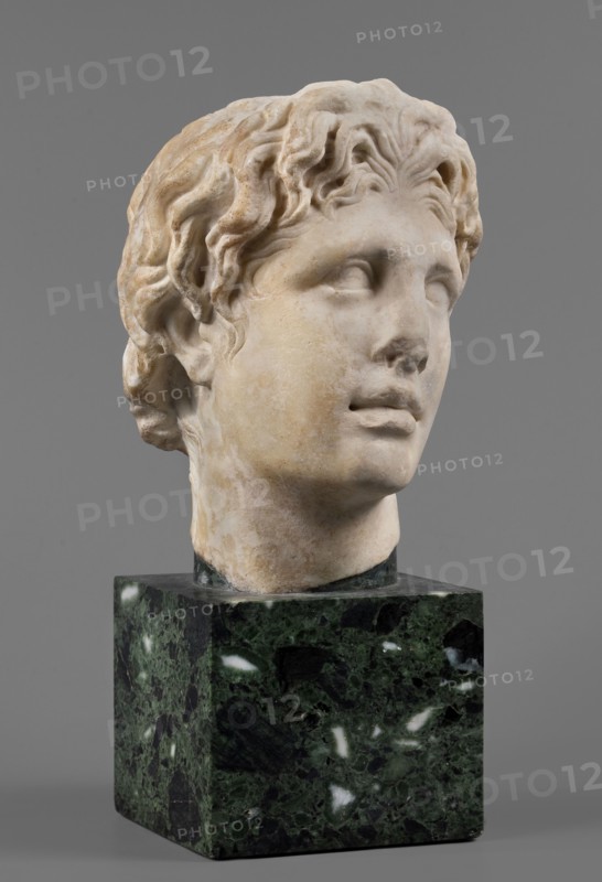 Head of Alexander the Great, unknown Roman workshop. Alexander III the Great King of Macedonia; 356–323 BC, male portrait, Roman sculpture, Roman copy from a Greek original, head. The head of a young man is clearly turned to the left in a pathetic manner. The head is reflected at the base of the neck. The face is oval, the skeletal structure is not emphasized. The mouth is prominent, with slightly parted lips. The nose is straight, reflected at the tip. The eyes are almond-shaped, deep-set, and the eyebrows are expressive, protruding strongly above the eyeball. The forehead is flat, low, and covered with lush locks of hair. The hairstyle consists of loosely arranged, slightly curled locks. Above the forehead, shifted off-axis to the right, a lock of hair is visible, radiating outwards, slightly raised and clearly different from the other locks. At the back of the head, the hair is arranged in wavy locks, with only the lower part being freely arranged. Dated 140–160 AD previously 150–16...