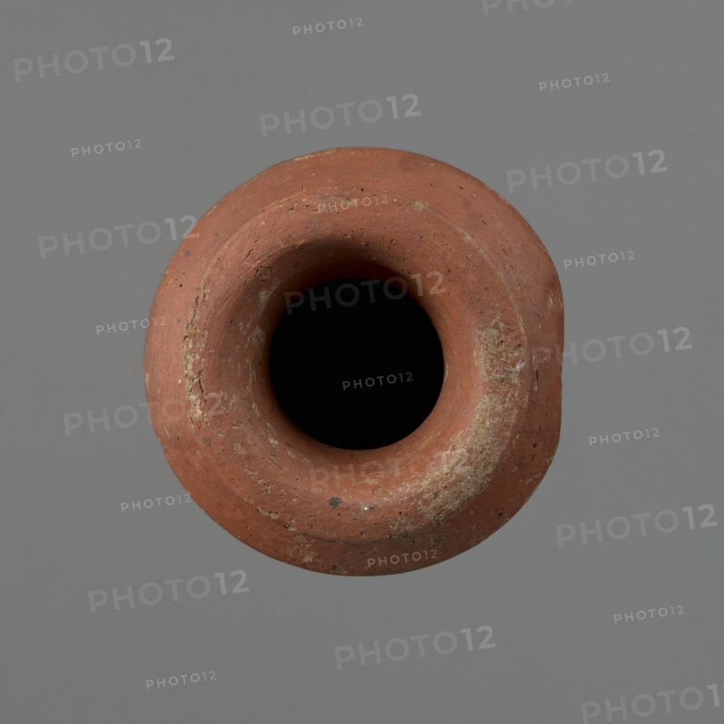 Vessel, Egyptian pottery, ceramics, clay vessel; conical-shaped vessel, widest at approximately 3/4 of its height. Quite wide, almost horizontal shoulders slightly sloping. Wide, short, funnel-shaped neck widening towards the spout. Wide spout, flat in the upper part, slightly rounded at the bottom, slightly asymmetrical. Flat, asymmetrical bottom. Surface leveled; lower part finished to approximately 2/3 of its height with a knife or similar tool. Outer surface and inner surface of rim and neck covered with a layer of dark red engobe. Vessel color dark red. Vessel complete; surface eroded in many places, numerous clay chips on the rim. Old Kingdom, ca. 2686–2181 BC; provenance Edfu. Height 16 cm; diameter 8.6 cm rim, 10.7 cm body, 4.5 cm bottom., A close-up top view of a round terracotta vessel with a wide rim and a deep dark interior, showing a weathered rough surface with patches of pale discoloration and small spots of darker tones, set against a smooth neutral gray background with...
