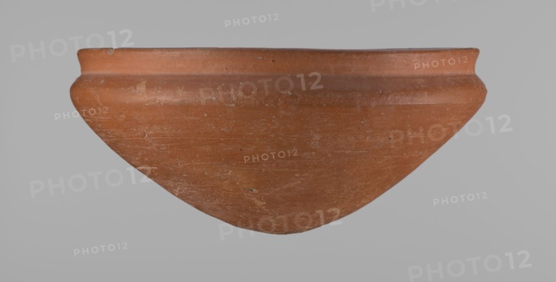 Medum type bowl, Ceramics; Egyptian pottery vessel Medum type bowl with carination under the rim. Rim diameter smaller than the diameter of the shoulders. Rounded bottom. Straight, slightly flaring rim. Made on the wheel from Nile clay; surface leveled. Bottom and lower part finished to about half its height with a knife or similar tool. Surface covered with a layer of engobe . Vessel color: red. Date: c. 2686–c. 2181 BC Old Kingdom. Origin: Edfu. Function: vessel. Height 9 cm; diameter rim 21.1 cm; diameter shoulders 21.5 cm., A large shallow bowl-like clay vessel is shown against a plain light gray background, with a rounded body tapering to a blunt point and a slightly flared rim; the surface shows a weathered texture with scratches and small chips. The predominant color of the vessel is terracotta, with lighter and darker variations of reddish-brown and some pale tan spots.