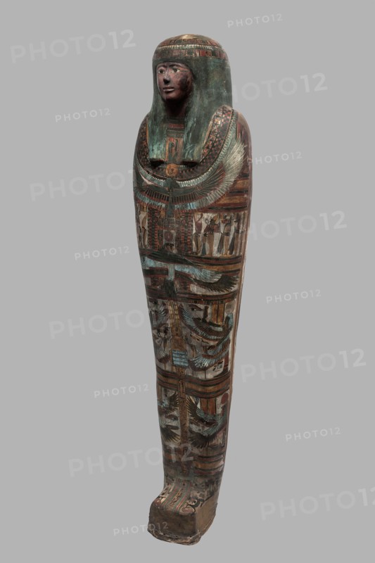 Mummy of Panepi in a cartonnage, doorkeeper of the temple of Amun Panepi, Panepi ca. 945–715 BC. Richly decorated cartonnage. The deceased's wig and mask are sculpturally detailed. On the chest is a necklace with a plant and geometric ornament. Below is a centrally located i3-w fetish mounted on a djed sign, behind which an inscription begins. On the sides of the fetish are winged goddesses Isis and Nephthys and the Horuses of Edfu. At the base of the fetish are depictions of Upwawet. Above the fetish is a ram-headed bird with outstretched wings Amun-Ra and Wadjet cobra, Osiris, and three Sons of Horus. The deceased's hands are not modeled. c. 825–715 BC; Third Intermediate Period, late 22nd–23rd Dynasty. Western Thebes. Sarcophagus, mummy, cartonnage. Height 170 cm; width 40 cm; depth 29 cm; weight 37.5 kg., The image shows a tall, narrow, full-length ancient coffin with a carved human face and wig, painted in muted greens, browns, reds, creams, and black; the face is reddish-brown wi...