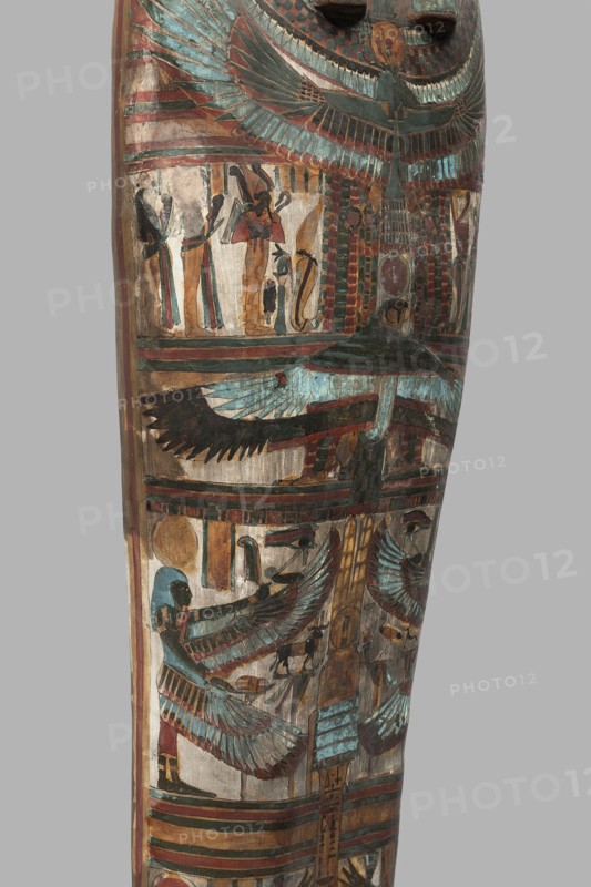 Mummy of Panepi in a cartonnage, doorkeeper of the temple of Amun Panepi, Panepi ca. 945–715 BC. Richly decorated cartonnage. The deceased's wig and mask are sculpturally detailed. On the chest is a necklace with plant and geometric ornament. Below is a centrally located i3-w fetish mounted on a djed sign, behind which an inscription begins. On the sides of the fetish are winged goddesses Isis and Nephthys and the Horuses of Edfu. At the base of the fetish are depictions of Upuaut. Above the fetish is a ram-headed bird with outstretched wings Amun-Ra and Wadjet cobra, Osiris, and three Sons of Horus. The deceased's hands are not modeled. c. 825–715 BC; Third Intermediate Period, late 22nd–23rd Dynasty; Western Thebes. Sarcophagus, mummy cartonnage. Height 170 cm; width 40 cm; depth 29 cm; weight 37.5 kg., A vertical painted wooden surface showing decorative figures and motifs with prominent winged shapes and stylized human figures, rendered in colors including turquoise, blue, green, r...