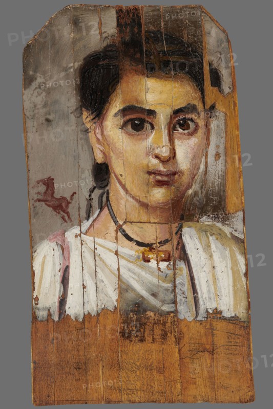Mummy portrait of a boy. Portrait of a boy painted on a small board with diagonally cut upper corners. The boy, shown halfway down his torso, has his head tilted slightly to the left. Lush black hair, combed upwards, falls behind his right ear, creating a lock of youth. Facial features are carefully depicted: large eyes with light brown pupils, precisely modeled; defined eyelashes; a long straight nose; a small mouth with slightly downturned corners. He wears a white tunic with a trapezoidal neckline, a purple clarus coat over his right shoulder, and a white cloak slung over his left. A black ribbon terminating in a gold pendant hangs around his neck. Above the right shoulder, against a light brown background, is the figurine of a small dark brown horse breaking into a gallop. The gray background around the head is carelessly painted, with visible brush marks. 2nd half of the 2nd century according to K. Parlaski, late 1st century, perhaps first half of the 2nd century. Egypt; Fayum. Po...