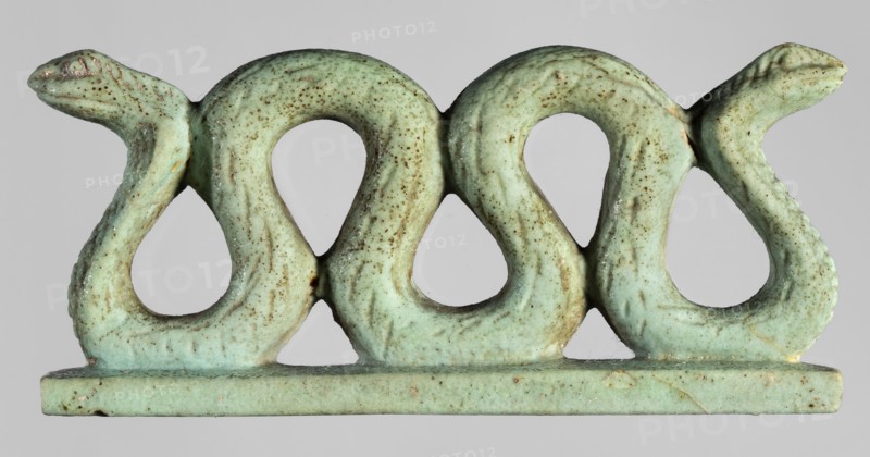 Amulet – two-headed snake;, Two-headed snake with vertical coils on a base, with delicately carved scales and snouts. Material: amulet. Function: protective amulet. Subject: snakes/animals. Style: Egyptian art. Date: 664–332 BC, Late Period, Egypt. Dimensions: height 3.3 cm, width 7 cm, depth 1.5 cm., A small sculptural object shaped like a horizontal row of three stylized looping serpents with raised heads at each end, rendered in a pale green color with a speckled brown patina and areas of slightly darker green; the piece sits on a flat rectangular base of the same pale green with brown speckling, and the background is a neutral light gray.